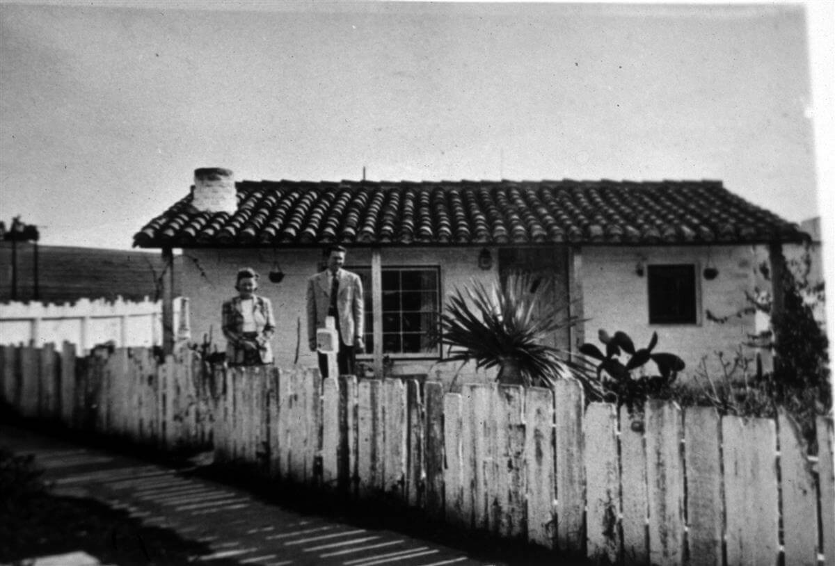 two people standing in front of an adobe house