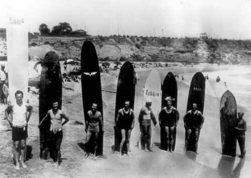 people standing in front of surfboards on the beach in 1928