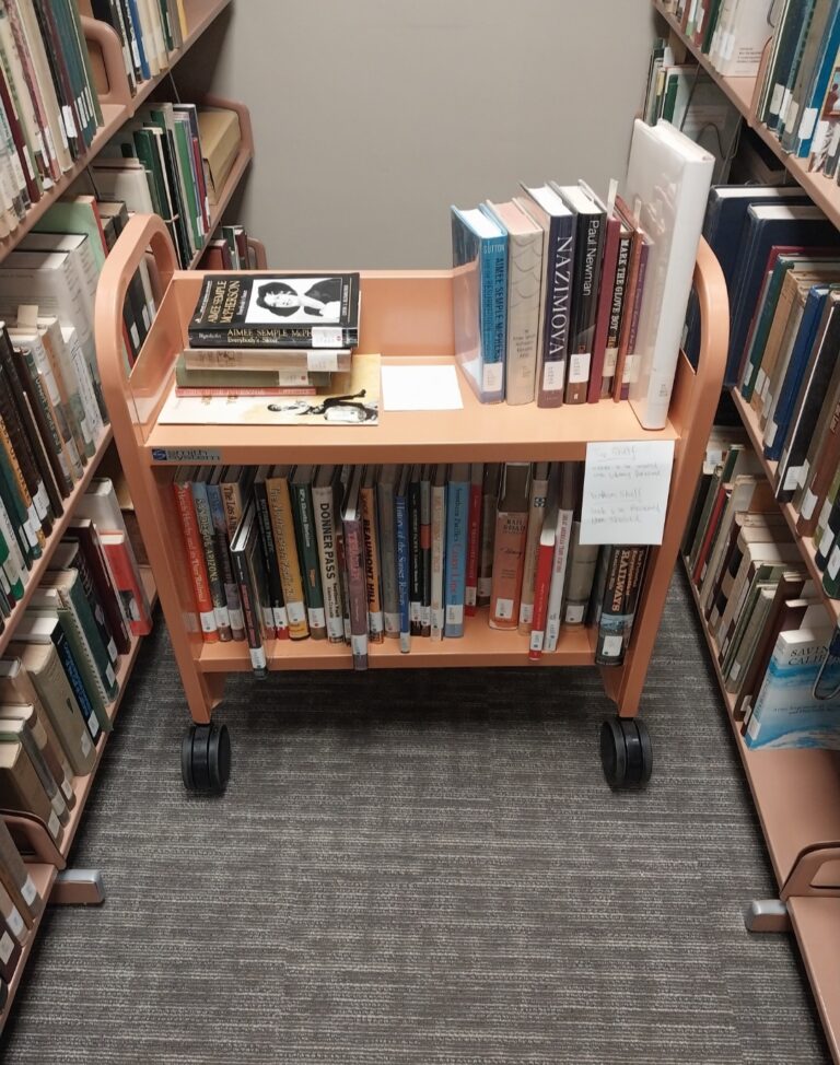 A wooden book cart filled with books from Sherman Library & Gardens