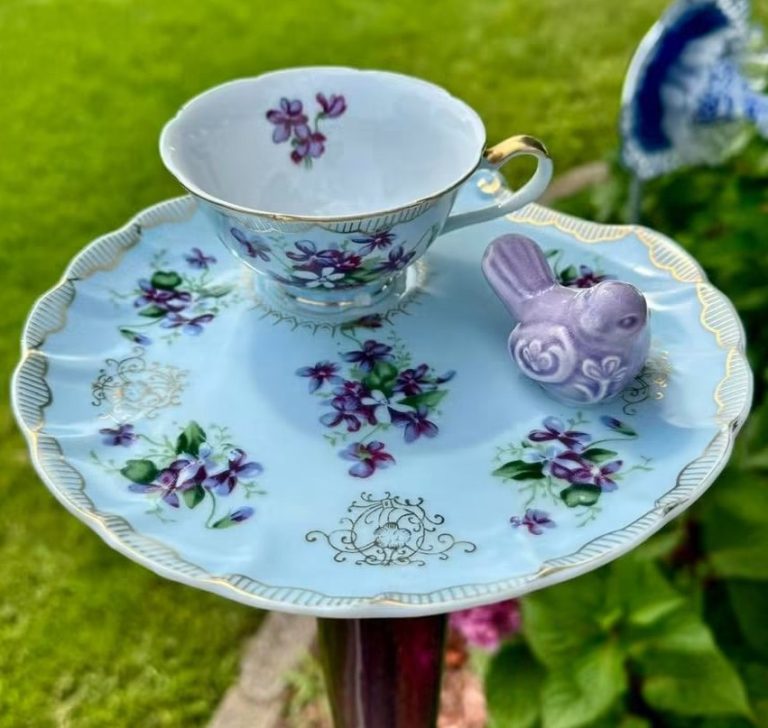A light blue teacup and saucer set decorated with violet flowers and a small purple bird figurine, mounted on a garden stake for the Sherman Sowers Gift Faire.