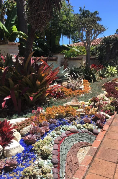 A xeriscaped garden features a decorative mosaic pathway curved through succulents and colorful rock accents.